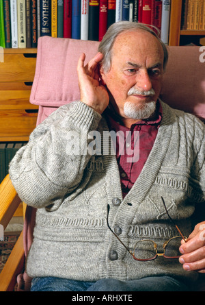 Il vecchio uomo senior con problemi di udito seduto su una sedia Foto Stock