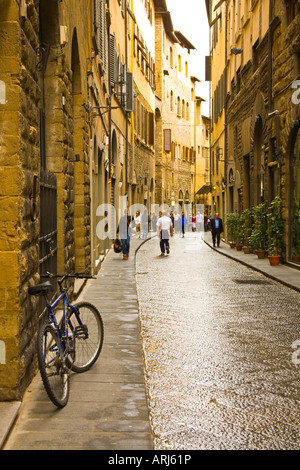 Un pedale abbandonati bike si appoggia contro una parete in una zona tranquilla di Firenze, Italia, street, mentre la gente del posto i turisti vagare intorno alle spalle. Foto Stock