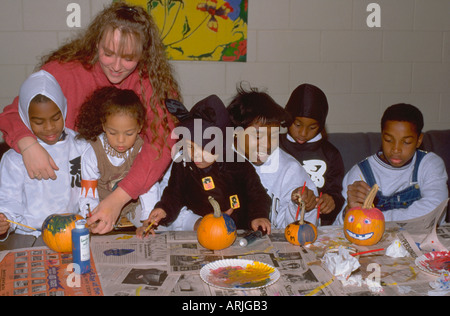 African American kids e mentor pittura zucche di Halloween party età 25 e 8 a 3. St Paul Minnesota MN USA Foto Stock