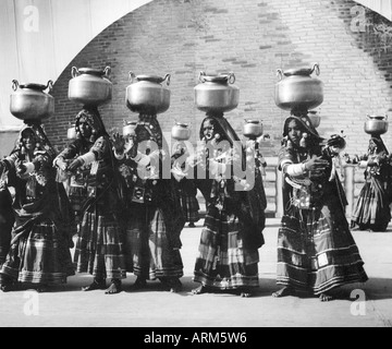 Le donne indiane in abito tradizionale azienda acciaio pentole di acqua sulla testa Foto Stock