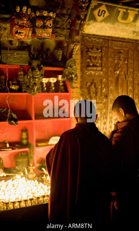I monaci luce di lampade a burro su una notte di buon auspicio, guardato da due maschere terribili, Boudha stupa, Bodhnath, Kathmandu, Nepal. Foto Stock