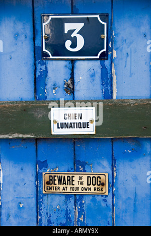 Colchester, Regno Unito. Vecchio Blu porta in legno con segni la lettura di "attenzione al cane' e Mad Dog' (in francese) Foto Stock