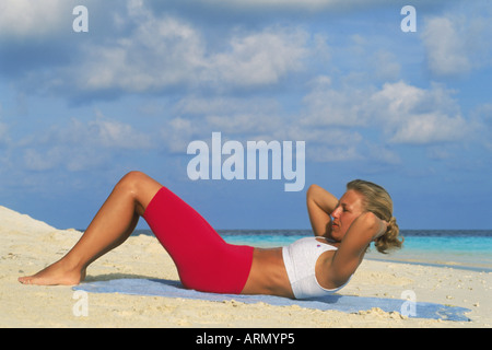 Donna facendo sit ups sulla spiaggia all'alba Foto Stock
