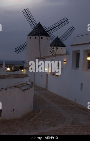 Due dei numerosi mulini a vento illuminate a giorno e a temperatura ambiente via acciottolata al crepuscolo e Campo de Criptana La Mancha Spagna Foto Stock