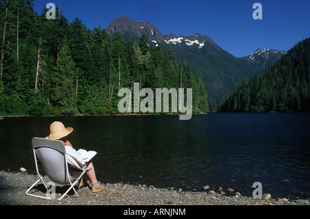 Schoen lago con la donna più anziana lettura sul litorale, Isola di Vancouver, British Columbia, Canada. Foto Stock