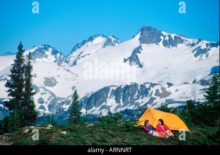 Coppia giovane nei campi a prato con sfondo di montagne di Whistler Alpine di Whistler, British Columbia, Canada. Foto Stock