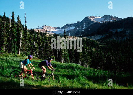 Coppia giovane giro in bici giù prato, Whistler, British Columbia, Canada. Foto Stock