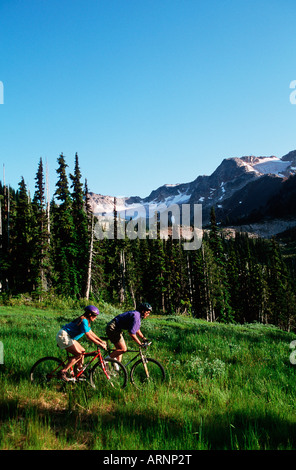 Coppia giovane giro in bici giù prato, Whistler, British Columbia, Canada. Foto Stock