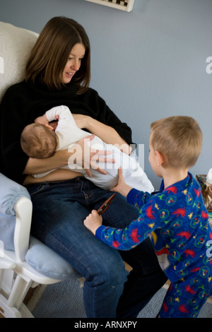 Tre anni di vecchio ragazzo cercando di ottenere attenzione dalla madre mentre lei è allattava il neonato Foto Stock