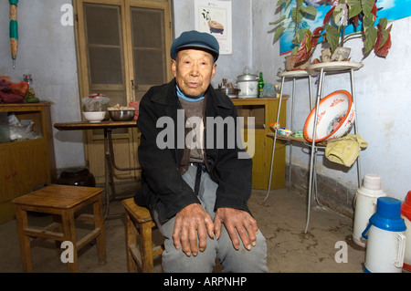 Anziani uomo cinese agricoltore seduto in agriturismo cucina nel borgo di poli vicino Penglai, Provincia di Shandong, Cina Foto Stock
