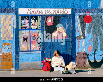 Villaggio di Kinvara, Baia di Galway, Irlanda. Donna legge turistica guida con cane nella parte anteriore della pittura murale di pesca shop. Foto Stock