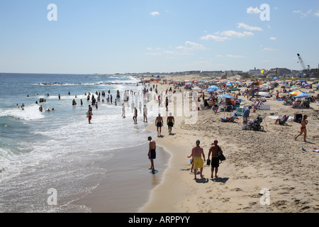 La gente camminare lungo la sabbia linea surf a ocean edge. Massa di pittoresca spiaggia ombrelloni e persone sulla sabbia appena sopra la linea di galleggiamento Foto Stock