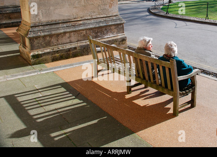 Due vecchie signore seduto sul banco di lavoro con lunga ombra. Foto Stock