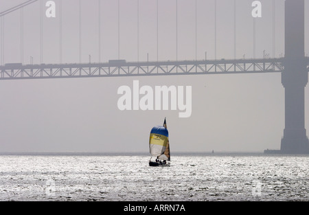 Un solitario vele yacht nella Baia di San Francisco con la retroilluminazione del Golden Gate bridge a distanza Foto Stock