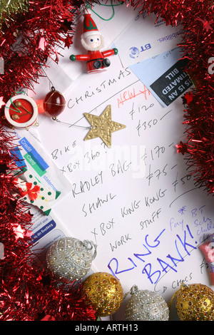 Fatture, estratto conto bancario, tinsel, albero decorazioni e carta di credito dichiarazioni circondano un regalo di Natale elenco. Foto Stock