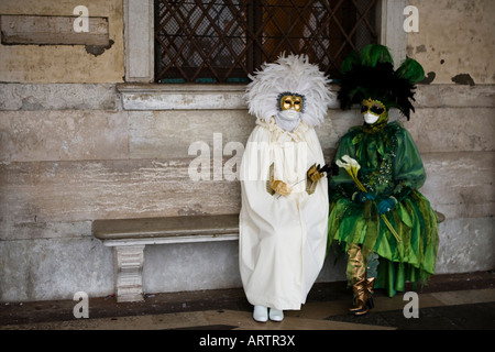 Due persone sedute su un sedile in pietra vestita di maschere e costumi di Carnevale di Venezia Veneto Italia Foto Stock
