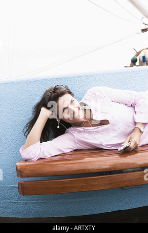 Ritratto di una metà donna adulta giacente su un banco di lavoro e di ascolto di un lettore MP3 Foto Stock