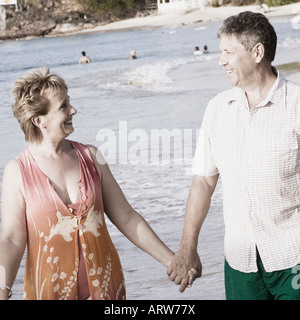 Donna matura tenendo un senior mano d'uomo e di camminare sulla spiaggia Foto Stock