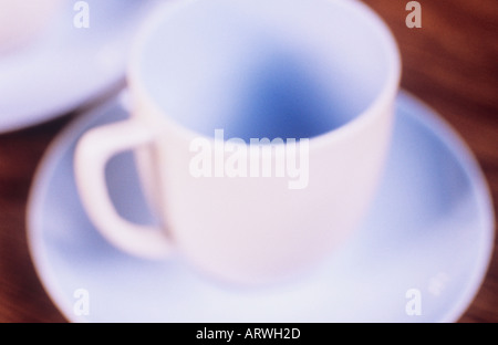 Impressionistica close up di un colore blu pallido e coppa piattino comunicante con un piattino o piastra su una tabella di colore marrone Foto Stock