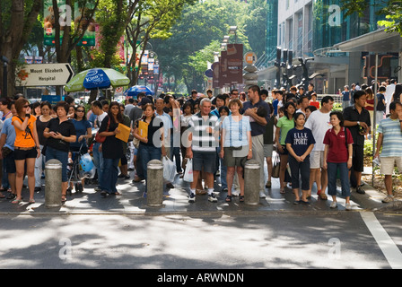 Una folla di persone attende pazientemente per la luce verde a camminare in modo sicuro attraverso la strada in Singapore occupato a Orchard Road e il quartiere dello shopping Foto Stock