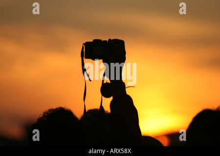 Persona prendendo foto sopra la folla al tramonto Foto Stock