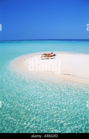 Giovane con sedie a sdraio su sandbar circondata dall'Oceano Indiano in Maldive Foto Stock