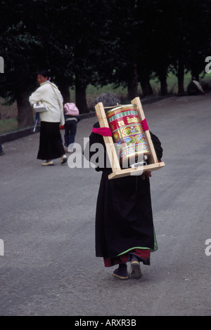Vecchia donna portando una grande preghiera ruota in Bamei Tagong praterie Tibet Kham Cina Sichuan 2004 Foto Stock