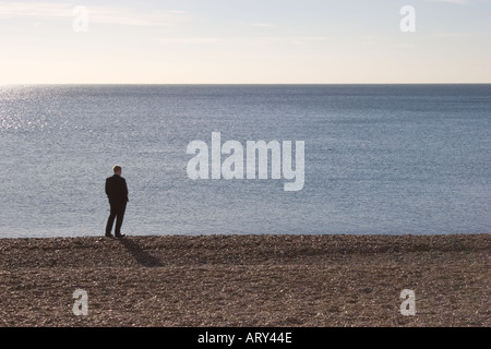 Lone uomo in piedi sulla spiaggia guardando fuori al mare a Brighton Regno Unito Foto Stock