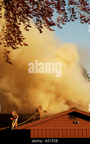 Flutti di fumo dal tetto di una casa come due vigili del fuoco battaglia blaze Foto Stock