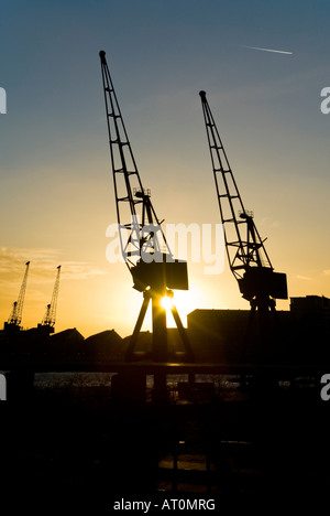 Vista verticale del sole che tramonta dietro le gru in disuso lungo il Royal Victoria Dock Foto Stock