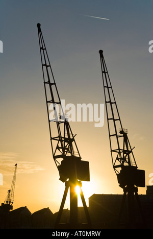 Vista verticale del sole che tramonta dietro le gru in disuso lungo il Royal Victoria Dock Foto Stock