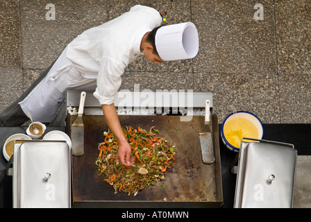 Antenna orizzontale in prossimità di uno chef in bianchi aggiunta di ingredienti per un preparato di fresco stir fry al di fuori su una piastra riscaldante Foto Stock