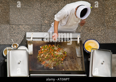 Antenna orizzontale in prossimità di uno chef in bianchi aggiunta di ingredienti per un preparato di fresco stir fry al di fuori su una piastra riscaldante Foto Stock