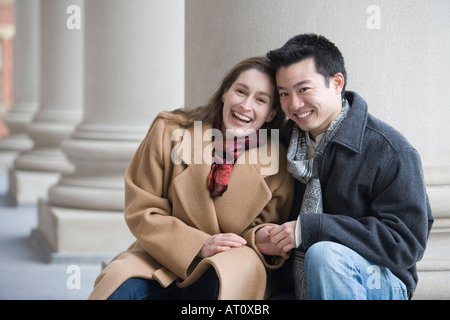 Ritratto di una giovane coppia seduta di fronte a una colonna e sorridente Foto Stock