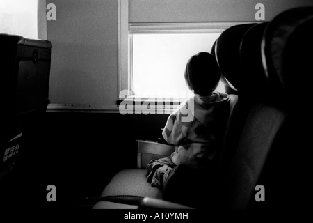 Ragazza giovane si inginocchia su un sedile in treno e guarda fuori la finestra del treno. Foto Stock