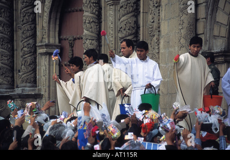 I sacerdoti benedizione offerte in miniatura con acqua santa fuori la chiesa di San Francisco, Alasitas festival, La Paz, Bolivia Foto Stock