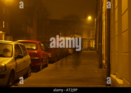 Giovane camminare sotto lampione sulle strette buio notturno di street a Belfast Foto Stock