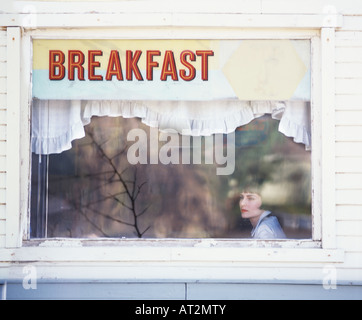 Moda donna di consumare la colazione in caffetteria guarda attraverso la finestra con riflessioni e cartello che dice che la colazione Foto Stock