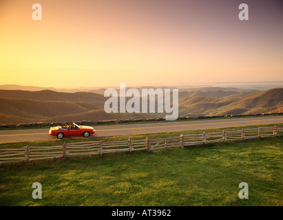 Un giovane in un convertibile guidare lungo la Blue Ridge Parkway al sorgere del sole con la Blue Ridge Mountains in background Foto Stock
