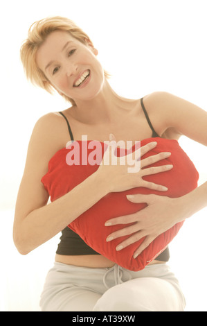 Una donna che abbraccia un cuore cuscino di forma Foto Stock