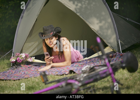 Un oscuro ragazza dai capelli in una tenda scrivere messaggi su un telefono cellulare Foto Stock