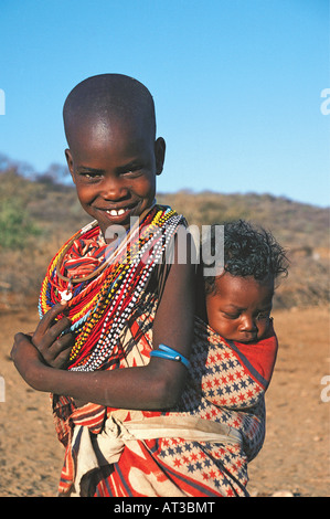 Giovane ragazza Samburu trasportare la sua sorella del bambino sulla schiena in villaggio nei pressi di Samburu Riserva nazionale del Kenya Africa orientale Foto Stock