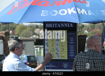 Bookmaker e il suo stand sotto un ombrello a Sandown Park Regno Unito Foto Stock