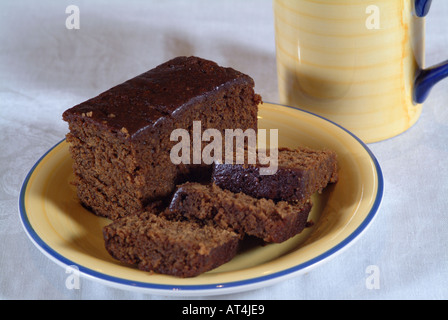 Parkin fette di torta e sulla piastra di colore giallo con la Tazza sul tavolo bianco panno Foto Stock