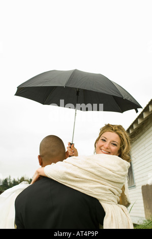 Lo sposo che trasportano sposa sotto ombrellone Foto Stock