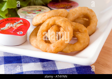 Una piastra di golden anelli di cipolla visualizzata con una gamma di confezioni di salse Foto Stock