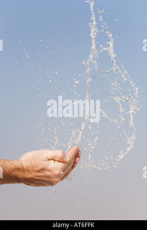 Acqua di essere gettato in aria da mani contro un cielo blu Foto Stock