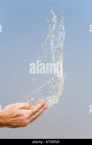 Acqua di essere gettato in aria da mani contro un cielo blu Foto Stock