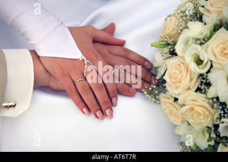 Un ritratto di una sposa giovane tenendo le mani per mostrare le loro fedi accanto a un mazzo di fiori sul womans w bianco Foto Stock