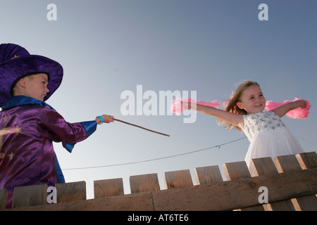 Procedura guidata di colata del ragazzo una magia con la sua bacchetta magica sulla ragazza bionda tenendo giù la boa nel vento Foto Stock